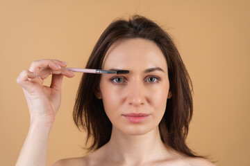 Close up beauty portrait of a woman with perfect skin and natural makeup, shiny lips, holding an eyebrow brush.