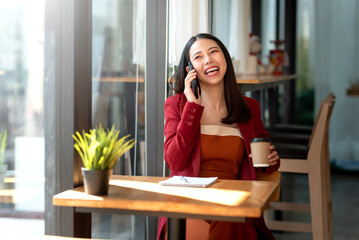 Confident Asian businesswoman in a red suit sitting talking on the phone with her client in café.