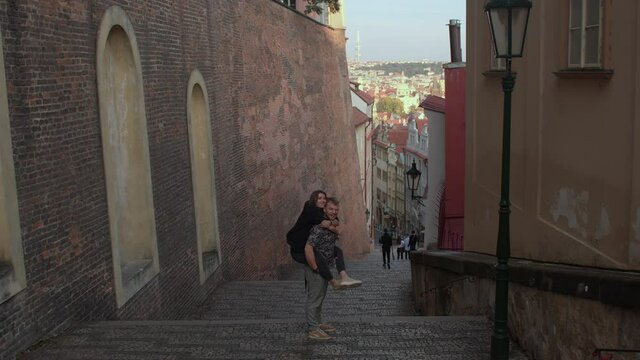 A man holds a woman on his back. Cheerful couple on the stairs in the old city. Positive motivation. Brick wall.