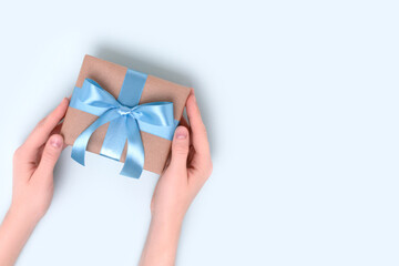 Female hands hold wrapped gift box on a blue background. Present tied with a ribbon. Festive composition with copyspace.