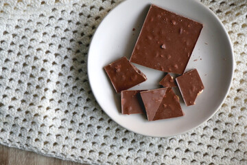 Almond and hazelnut chocolate bar on a plate and soft knited blanket. Top view.