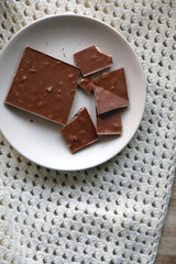 Almond and hazelnut chocolate bar on a plate and soft knited blanket. Top view.