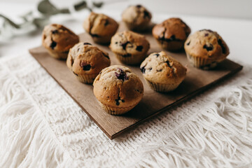 Homemade muffins with blueberries on brown wooden board on white table, boho napkin, leaves. Tasty cakes, sweets, cupcakes. No sugar, free gluten. Receipt of keks. Sweet dessert buffet. Holiday.