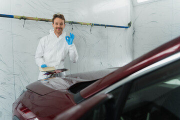 Satisfied car painter with color samples in hand shows ok gesture