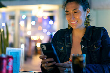 young latin woman looking at mobile device in a restaurant or pub portrait.