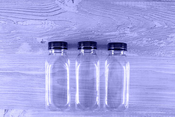 Three plastic transparent empty bottles with a black cap on a wooden table. There is a place for your logo. Very Peri toned image. copy space