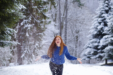  girl with red hair, throws snow, joyfully. in a blue sweater, playing