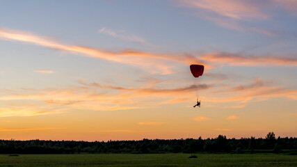 Obraz premium Beautiful scenic sunset with silhouette of powered paraglider pilot on the cloudy sky coloured by the sun