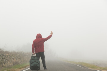 Persona andando  de espalda entre la niebla con chaqueta roja y maleta a cuestas en  invierno por...