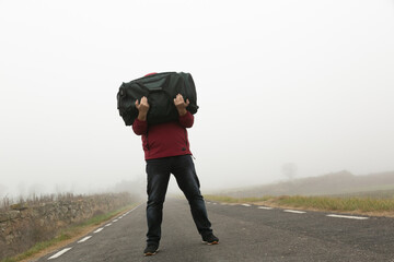 Cargando una maleta en los brazos un hombre irreconocible caminando por una carretera en un día...