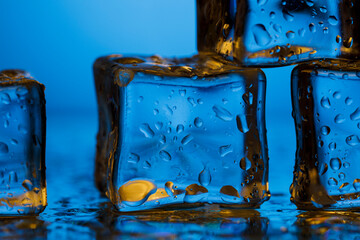 Ice cubes and water drops in close-up on a blue background.