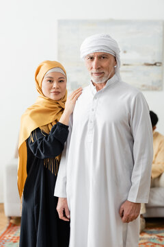 middle aged interracial couple in traditional muslim clothes looking at camera.