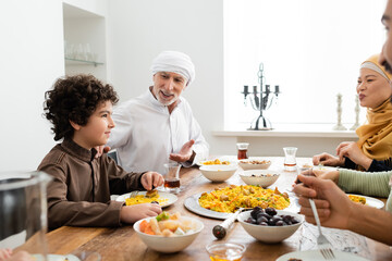 middle aged muslim man pointing at arabian grandson during family dinner with interracial family.