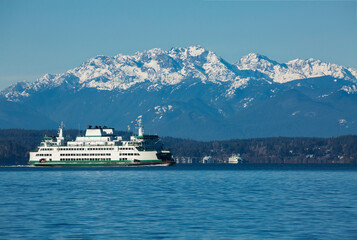 Fototapeta na wymiar A ferry boat moves on Puget Sound with snow-capped Olympic mountains in the background on a winter day in Seattle, WA 