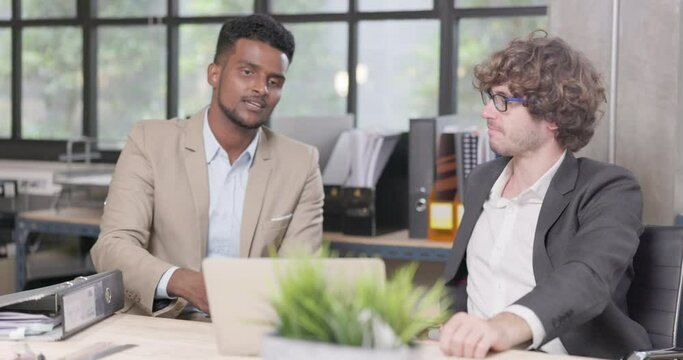 Two male coworkers in the office conversing and working together at work, happy businessmen teammates discussing computer business project brainstorming in corporate teamwork