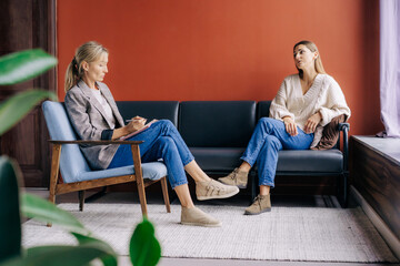 A female psychotherapist during a visit attentively listens and counseling a young woman talking...