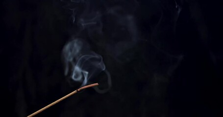 Smoke rises in slow motion from a burning incense stick as ashes build up and then fall