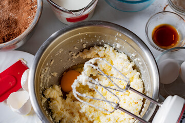 Making a chocolate cake:  Adding an egg, one at a time.  Overhead angle with additional ingredients surrounding mixing bowl.