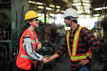 A smiling female engineer shakes hands to greet a tall, handsome, dark-skinned engineer while working in an industrial factory.Teamwork and gender diversity concept