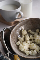 Milk kefir grains in a gray plate with a bottle and a cup of kefir on white table.