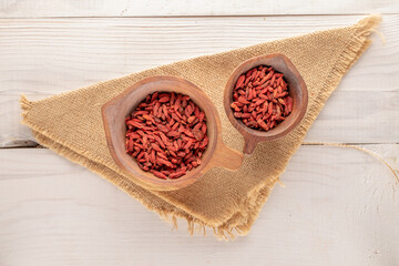 Dried organic goji berries in two wooden cups with a burlap cloth on a wooden table, macro, top...