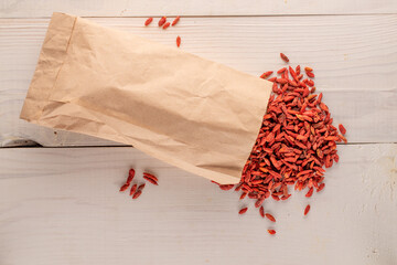 Dried organic goji berries in a paper bag on a wooden table, macro, top view.
