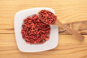 Dried organic goji berries on a white saucer on a wooden table, macro, top view.