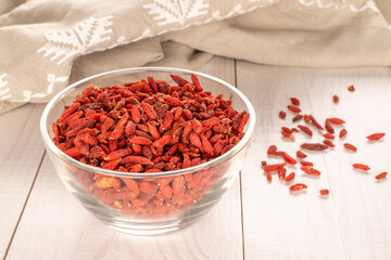 Dried goji berries in a glass dish on a wooden table, macro.