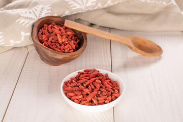 Dried goji berries in a white saucer and in a wooden cup with a wooden spoon on a wooden table, macro.