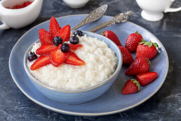 Creamy Rice Pudding with fresh sliced strawberries and blueberries served in ceramic bowl with whole berries and sauce on table