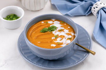 Sweet potato pumpkin vegetable soup with coconut cream and basil leaves on on white stone background.
