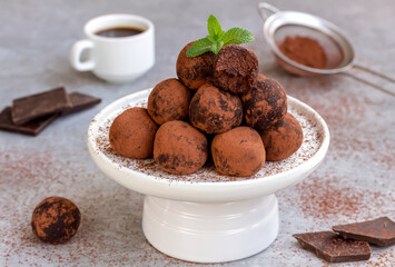 Chocolate Coffee Truffles. Assorted chocolate candy balls served on white serving stand with cocoa, cup of coffee and chocolate pieces on background. 