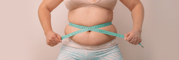 fat woman, fat belly, plump, obese woman holding excess belly fat with measuring tape on beige background, female diet lifestyle concept