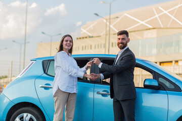 The male car salesman hands over the keys to the female buyer, the purchase agreement is successfully completed