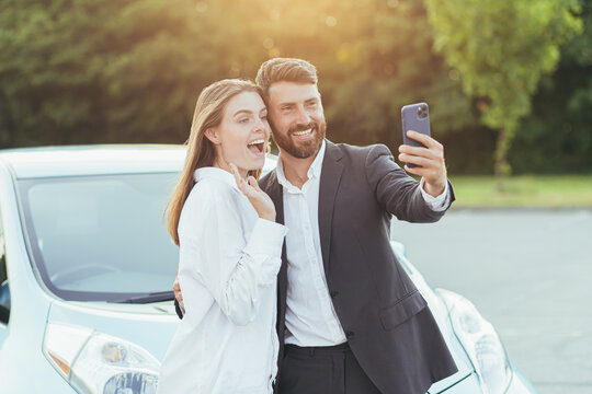 Young beautiful couple man and woman, happy to buy a new car, take photos together on the phone, and show friends shopping by video call