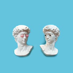 two antique copy Plaster sculpture  heads  with google eyes and pink hearts on eyes on blue...
