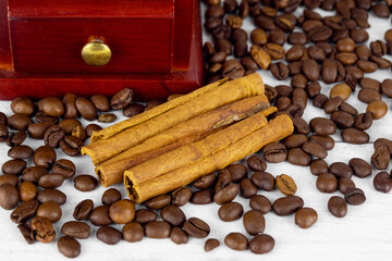 Three cinnamon sticks on coffee beans near wooden coffee grinder drawer