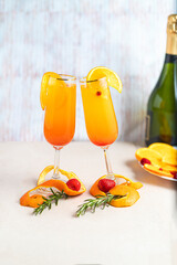 Glass with mimosa cocktail with orange and champagne decorated with strawberries, orange peel, leaves and currants inside the glass on a light background, vertical position