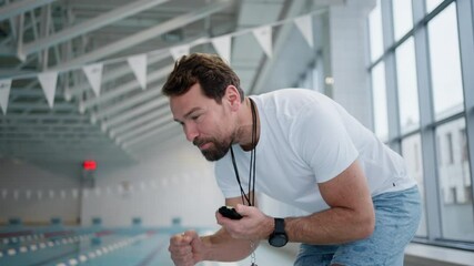 Personal coach encouraging swimmer when swimming indoors in swimming pool.
