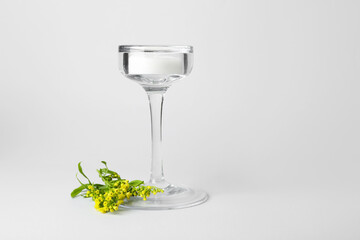 Candle with glass holder and flowers on light background