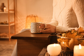 Woman with cup of coffee and autumn leaves at home, closeup