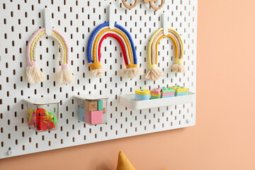 Peg board with toys hanging on beige wall, closeup