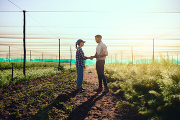 You're doing a fantastic job. Full length shot of two young farmers shaking hands while working on their farm.