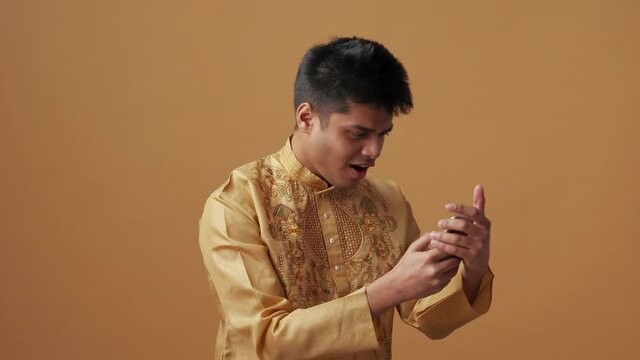 Cheerful Indian man in national cloth looking at phone in the orange studio
