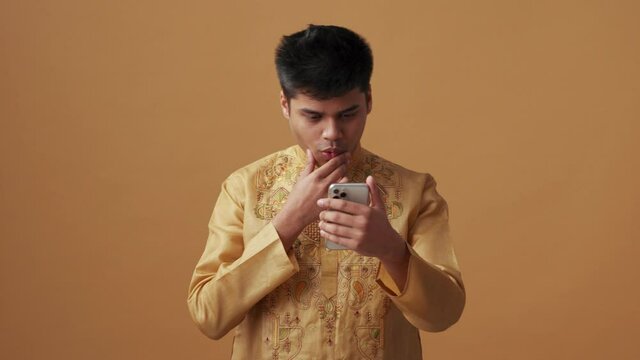 Happy Indian man in national cloth looking at phone in the orange studio