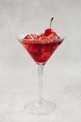 Glass of iced Manhattan cocktail with cherry on light background
