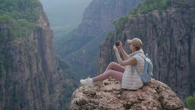 A tourist at the view point of the Tazy Canyon. A girl takes pictures of the stunning canyon landscape on her smartphone.