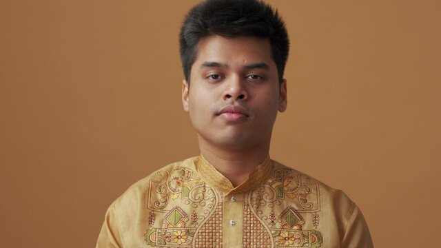 Positive Indian man in national cloth opening his eyes at the camera in the orange studio