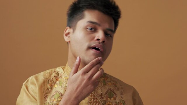 Serious Indian man in national cloth correcting his appearance at the camera in the orange studio