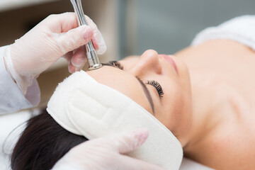 lovely female doing radiofrequency procedures on her face by a cosmetologist in a wellness center....